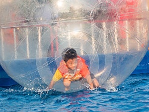 Young Asian boy playing inside a floating water walking ball