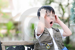 Young Asian boy sitting on the chair in the garden. Exploring the world, outdoor activity. Feeling confuse and sleepy