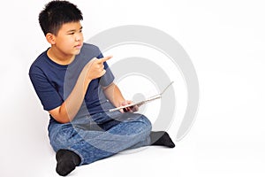 Young asian boy sitting cross-legged, holding a book and point to the side. Education concept