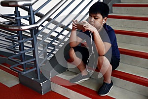 Young Asian boy sitting on stairs using smartphone with ear phones