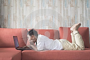 Young asian boy using laptop computer lying on a sofa at home.