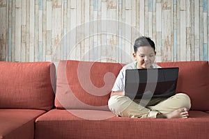 Young asian boy using laptop computer on a sofa at home.