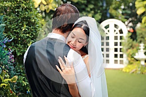 Young asian bride in white wedding dress is hugging his husband caucasian groom with love while close her eyes and happiness