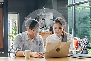 Young Asian business couple using laptop computer working together in coffee shop. college student discussing to project planning