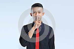 Young asian business man asking to be quiet with finger on lips. Silence and secret concept
