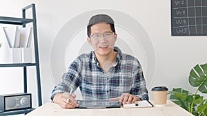 Young Asian business man attend to remote video call conference meeting, look at camera, use digital tablet in home office