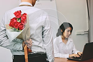 Young Asian business man holding a bouquet of red roses behind his back for girlfriend in valentines day. Love and romance in work