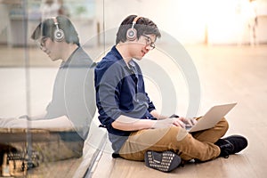 Young Asian business man listening to music while using laptop