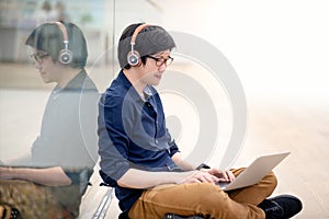 Young Asian business man listening to music while using laptop