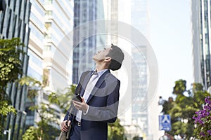 Young asian business man looking up at tall buildings in downtown