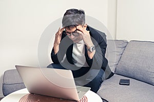 Young Asian business man sitting on sofa and working from home. Man feeling stress and suffering from headache. Tired young