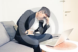 Young Asian business man sitting on sofa and working from home. Man feeling stress and suffering from office syndrome with