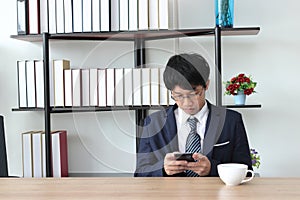 Young Asian business man using mobile smart phone in hands in office