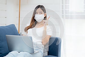 Young asian business woman in face mask think idea and work from home on laptop computer online to internet in living room.