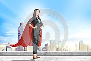 Young asian business woman with red cape standing on the rooftop