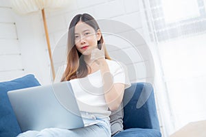 Young asian business woman smile and work from home with laptop computer online to internet on sofa in living room.
