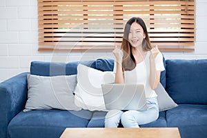 Young asian business woman smile and work from home with laptop computer online to internet on sofa in living room.