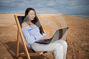 Asian business woman with tablet computer during tropical beach vacation. Freelancer working on laptop lying on sun lounger.