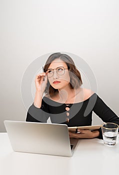 Young asian business woman thinking daydreaming sitting at desk with laptop computer