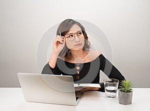 Young asian business woman thinking daydreaming sitting at desk with laptop computer