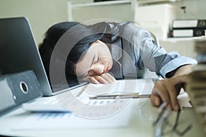 Young asian Business woman tired woman sleeping on desk with laptop at workplace alone.