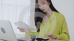 Young asian business woman using calculator with calculate tax for chart and graph report of earning home.