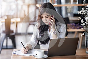 Young asian business woman using laptop and writing on notebook