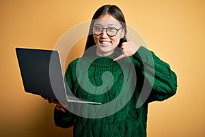 Young asian business woman wearing glasses and working using computer laptop smiling doing phone gesture with hand and fingers