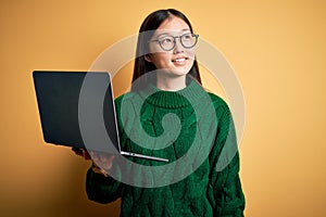 Young asian business woman wearing glasses and working using computer laptop smiling looking to the side and staring away thinking