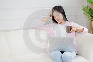 Young asian business woman work from home with laptop computer and drinking coffee on sofa in living room.