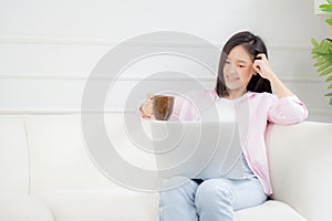 Young asian business woman work from home with laptop computer and drinking coffee on sofa in living room.