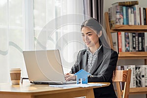 Young Asian business woman working in the office and using her laptop in her office with paper house