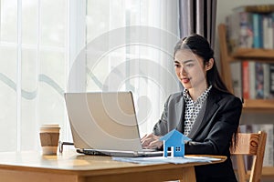 Young Asian business woman working in the office and using her laptop in her office with paper house