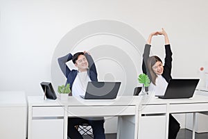 Young Asian businessman and businesswoman relaxing stretching arms, head and hands after work with laptop for a long time