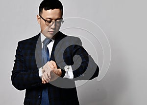 Young asian businessman expert in official jacket, tie and glasses stands looking at his watches checking time