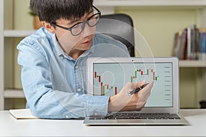 Young Asian businessman or investor pointing on stock tickers or Cryptocurrency trading graphs to teach about investing new stock
