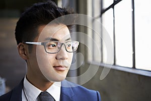 Young Asian businessman looking out of window, close up