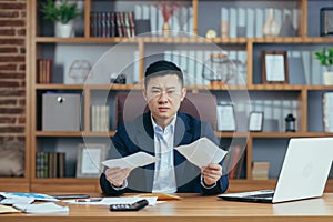 Young asian businessman man, banker, director sitting at desk in office, holding bills, documents, embarrassed, serious, waving