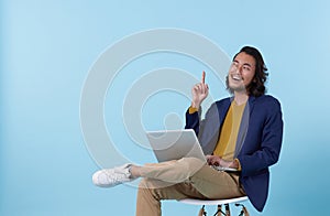 Young asian businessman thinking. While her using laptop sitting on  chair and looking isolate on blue background