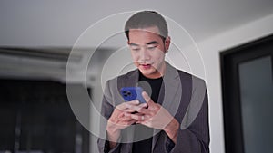 Young Asian businessman typing messages or reading news on his smartphone