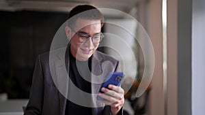 Young Asian businessman typing messages or reading news on his smartphone