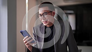 Young Asian businessman typing messages or reading news on his smartphone