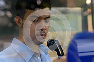 Young Asian businessman using the payphone outdoors