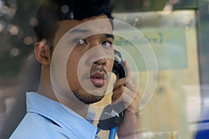 Young Asian businessman using the payphone outdoors