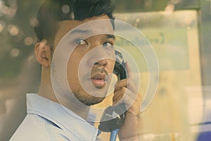 Young Asian businessman using the payphone outdoors