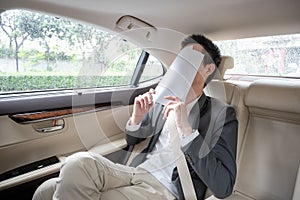 Young asian businessman using tablet and looking out of window while sitting on the back seat in the car.