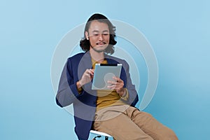 Young asian businessman using tablet sitting on chair isolate on blue background