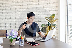 Young asian businessman wear casual clothing while sitting in modern kitchen near window, working with computer laptop at home.