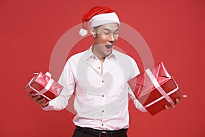 Young asian businessman wearing Santa hat and holding gift box in christmas and happy new year party on red background