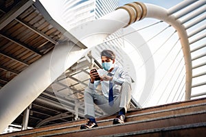 Young Asian Businessman Wearing a Surgical Mask and Using a Smart Phone in City. sitting on Staircase. Healthcare in New Normal